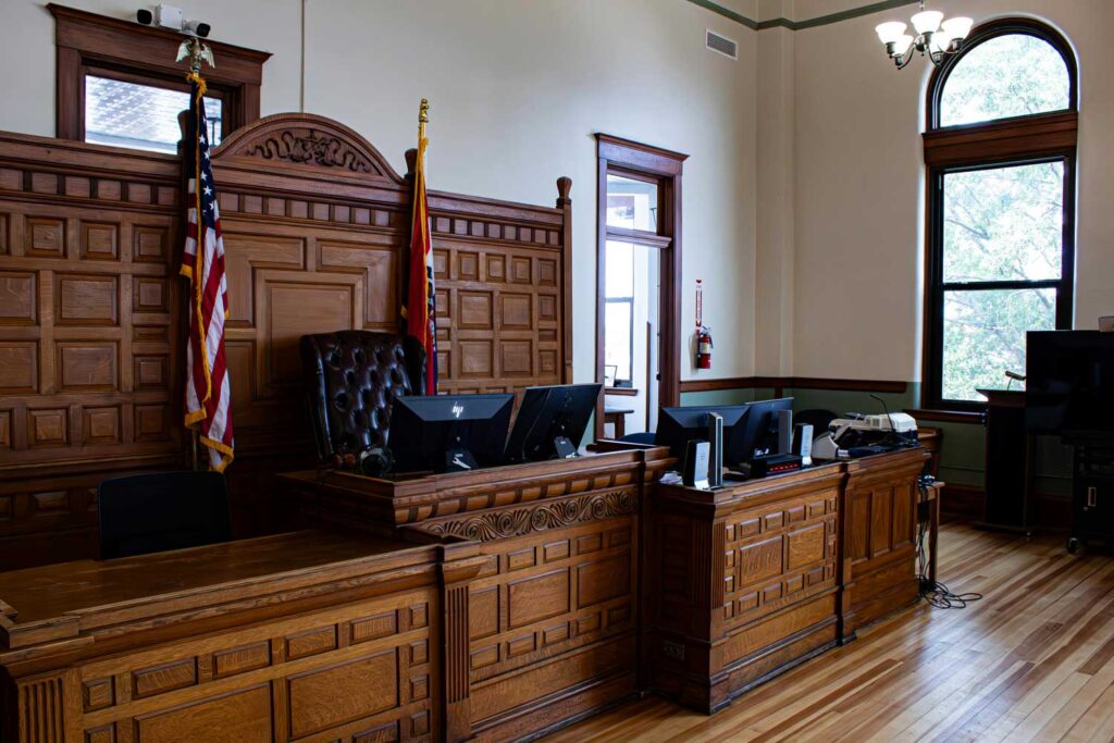 An empty courtroom with flags on either side of the judge's seat