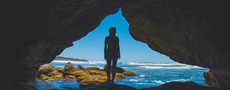Woman standing in cave near ocean